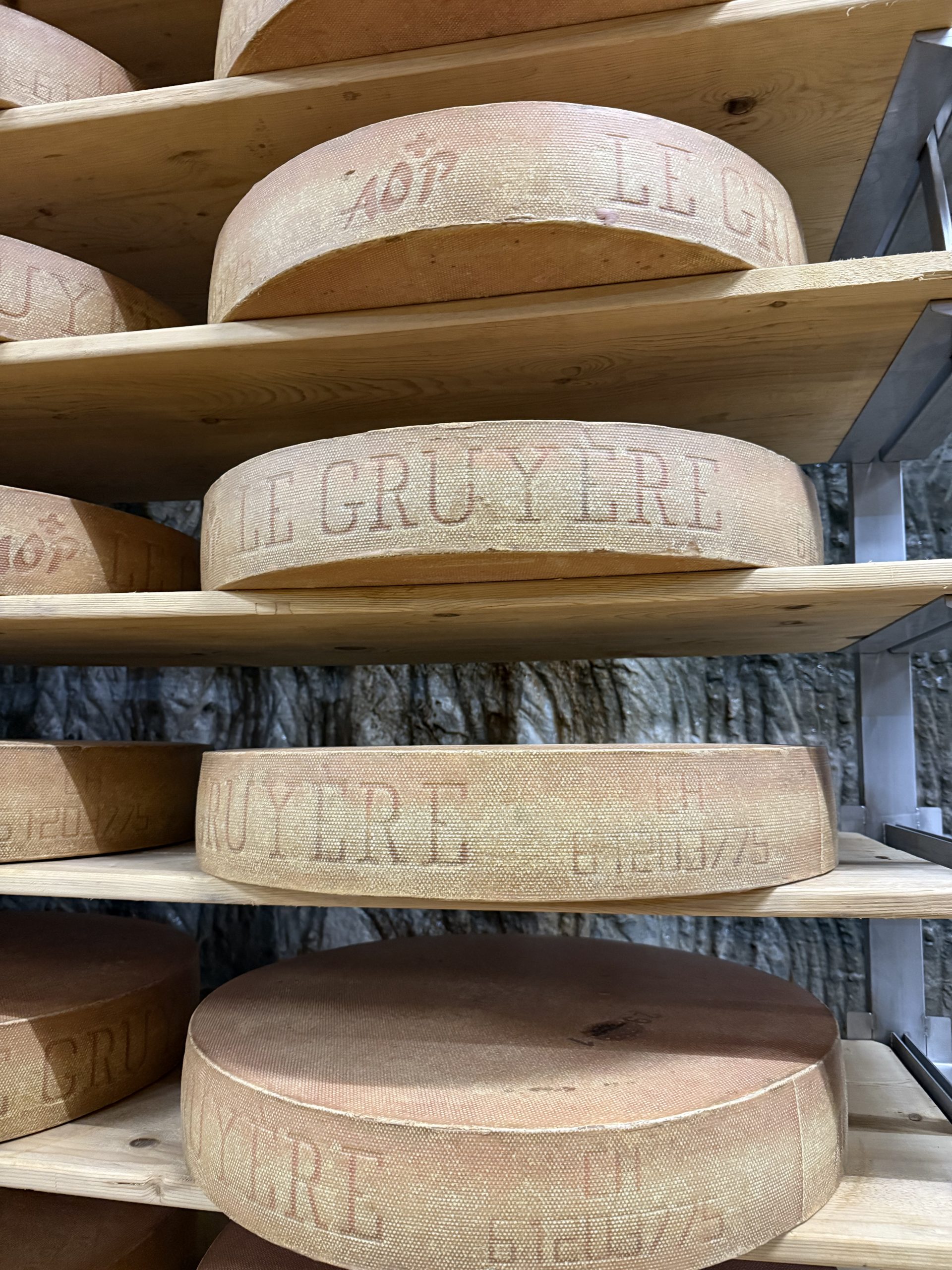 The picture shows wheels of Le Gruyère AOP maturing on wooden shelves inside the Kaltbach caves