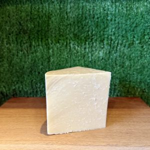 A picture of a wedge of Yorkshire Wensleydale PGI. It is positioned on a wooden board with a green background