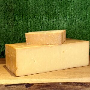A picture of a block of Smoked Cheddar. It is on a wooden board with a green background