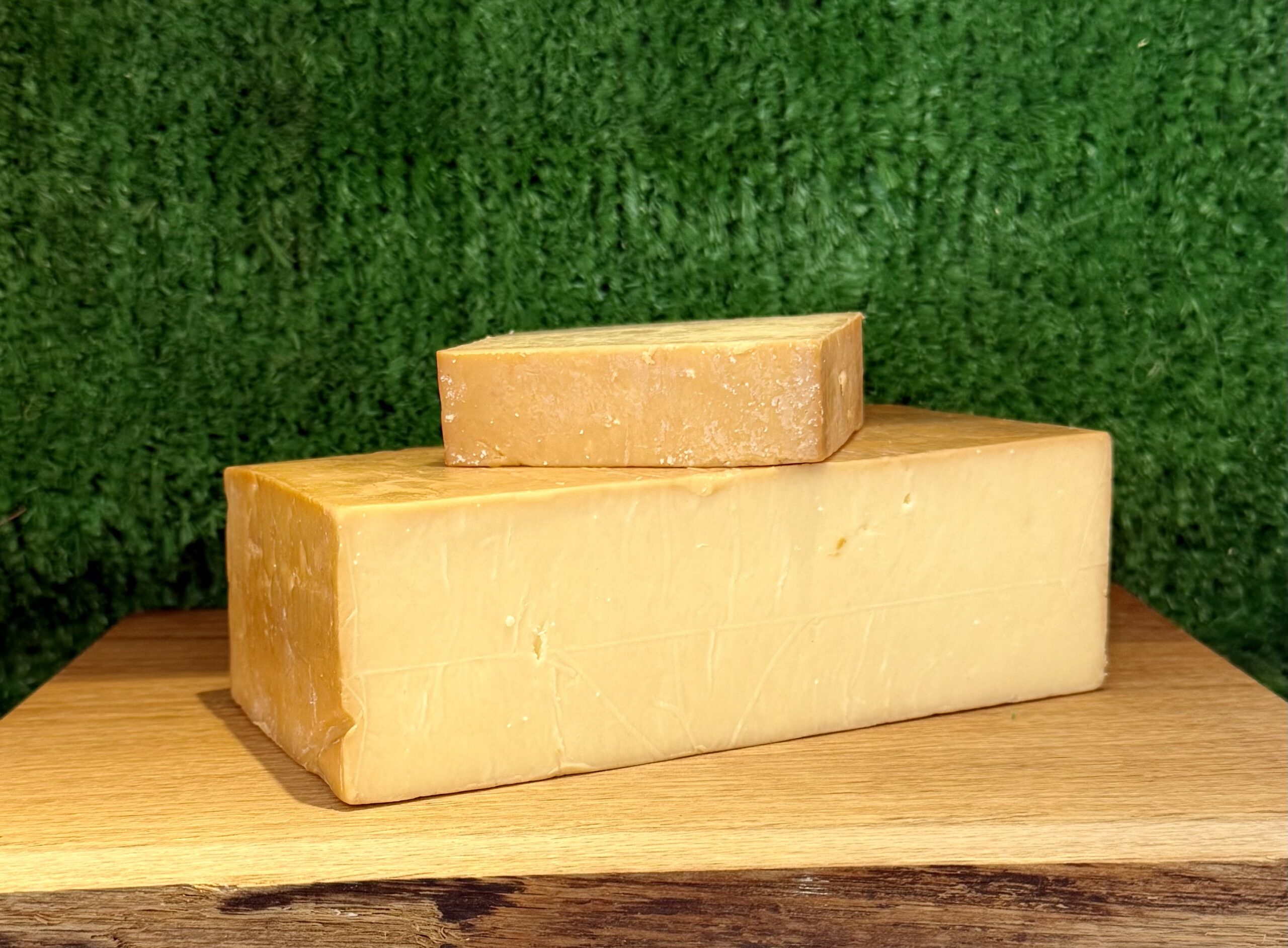 A picture of a block of Smoked Cheddar. It is on a wooden board with a green background