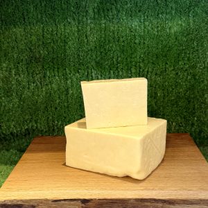 A picture showing 2 pieces of Barber's 1833 Vintage Reserve Cheddar. They are positioned on a wooden board with a green background