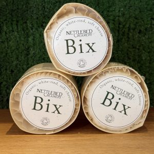 A photo showing 3 Bix cheeses arranged as a pyramid. They are positioned on a wooden board with a green background