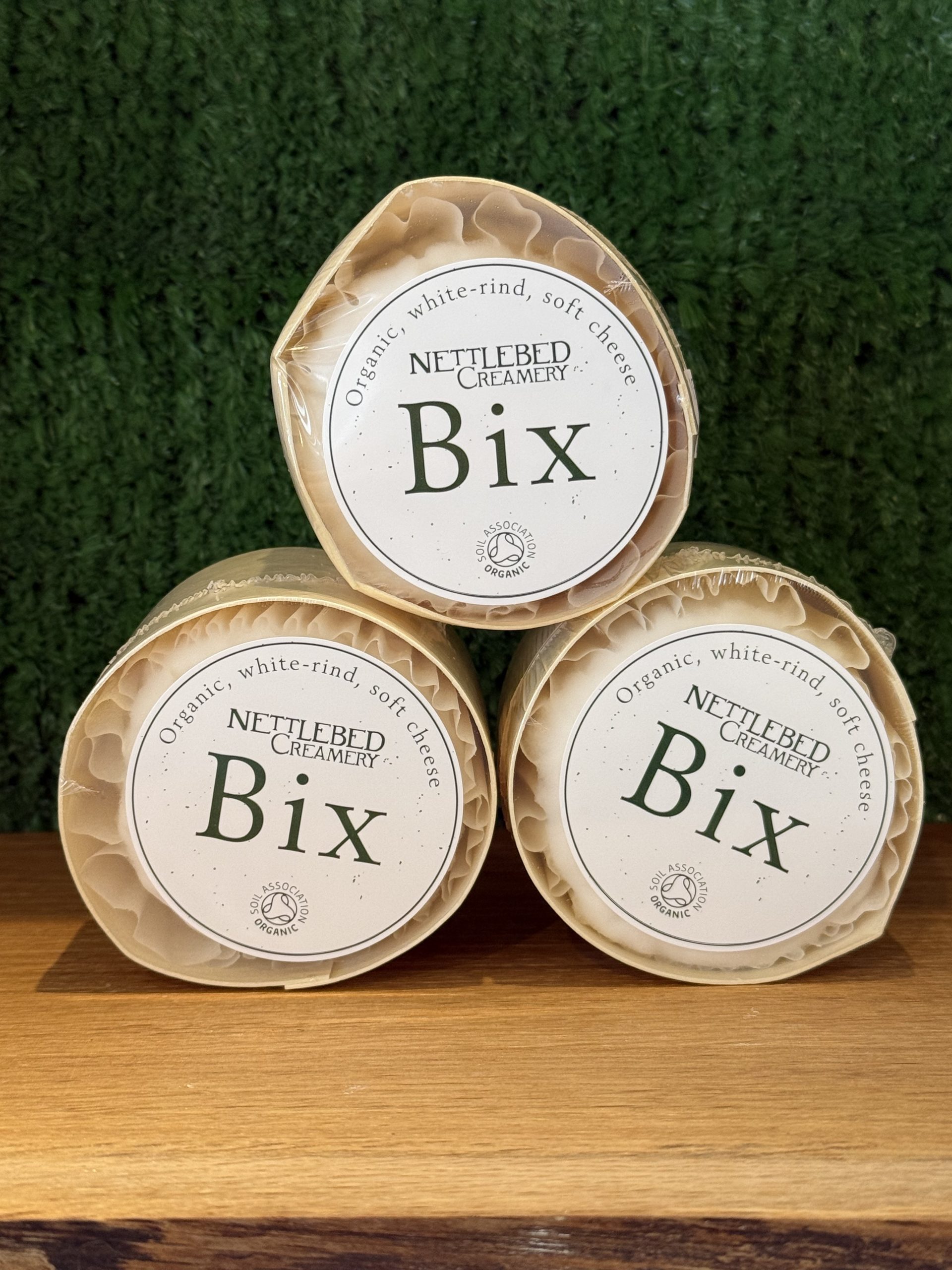 A photo showing 3 Bix cheeses arranged as a pyramid. They are positioned on a wooden board with a green background