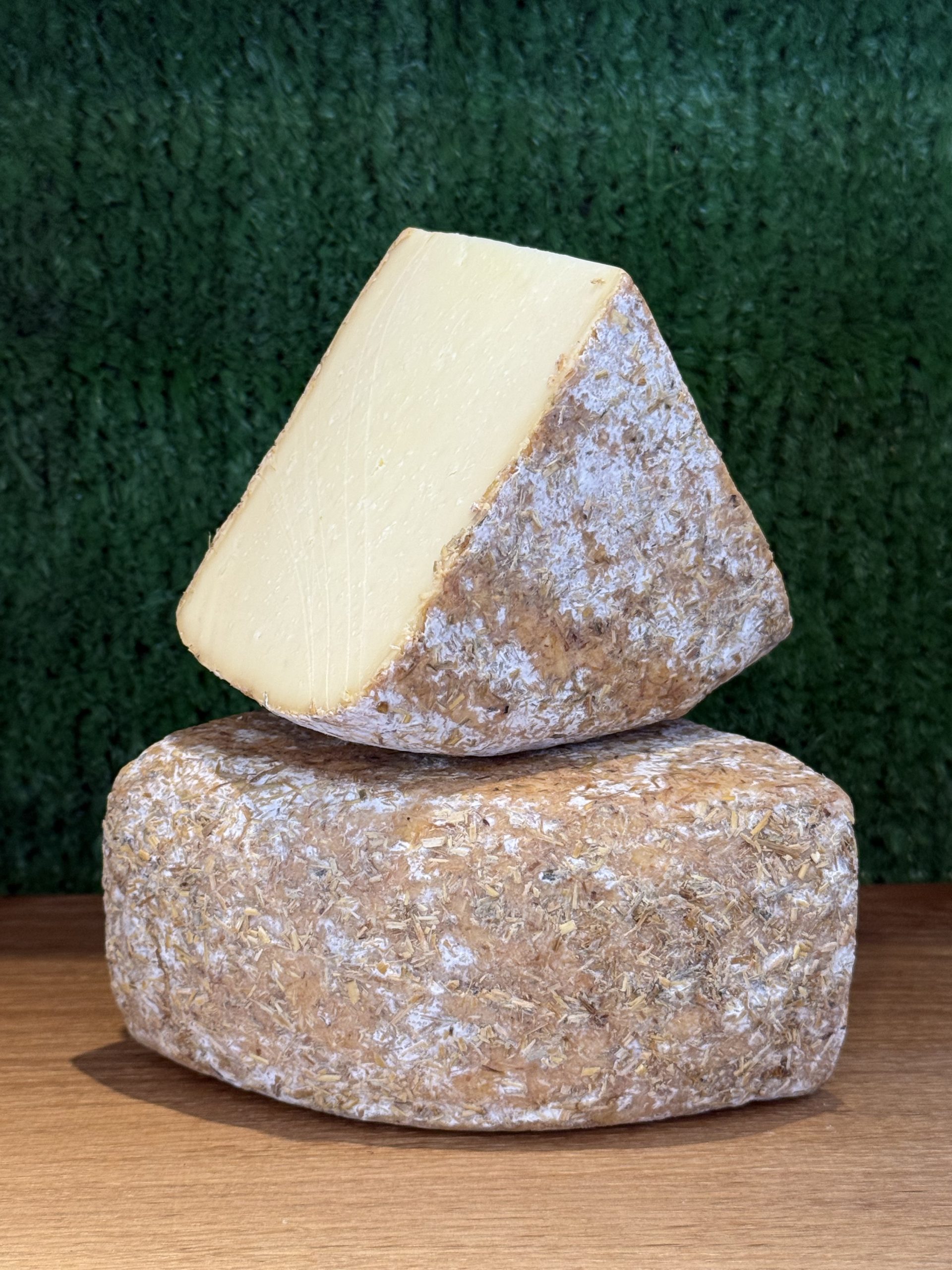 A photo showing 2 wedges of Witheridge cheese. One is balanced on the other at a jaunty angle. They are positioned on a wooden board with a green background