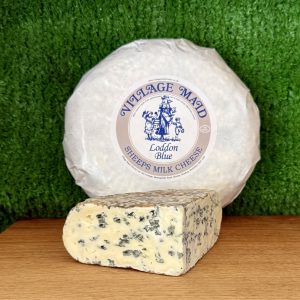 A picture showing a wedge of Loddon Blue. It is sat on a wooden board with a whole round of cheese propped up behind it