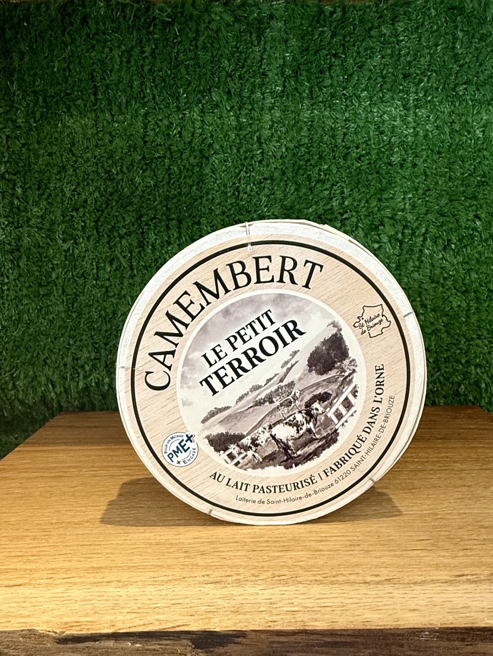 A picture of a boxed Camembert Le Petit Terroir. It is on a wooden board with a green background