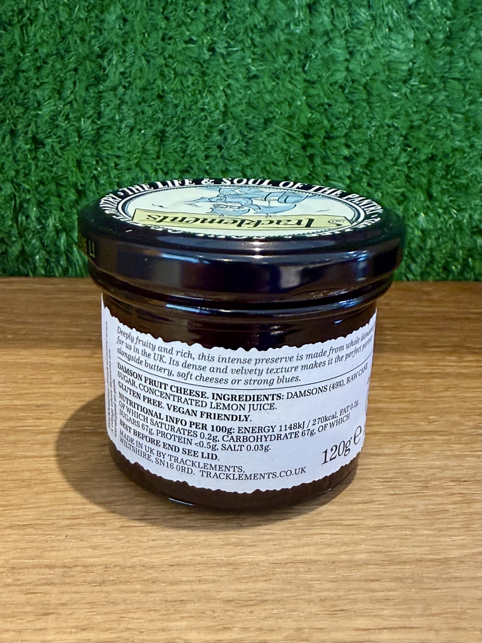 A picture of the back of a Damson Fruit Cheese jar. It has been placed on a wooden board with a green background