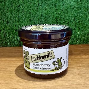 A picture of a jar of Tracklments Gooseberry Fruit Cheese. It is shown on a wooden board with a green background