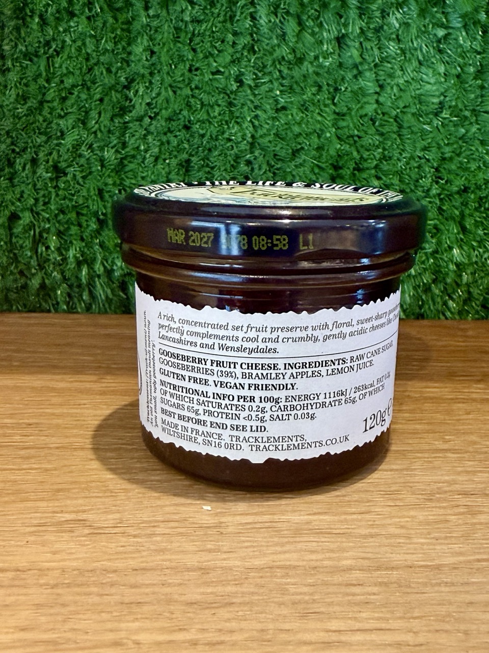 A picture of the back of a gooseberry fruit cheese jar. It is sat on a wooden board with a green background