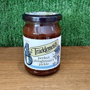 A photo of a jar of Perfect Ploughman's Pickle. It is pictured on a wooden board with a green background