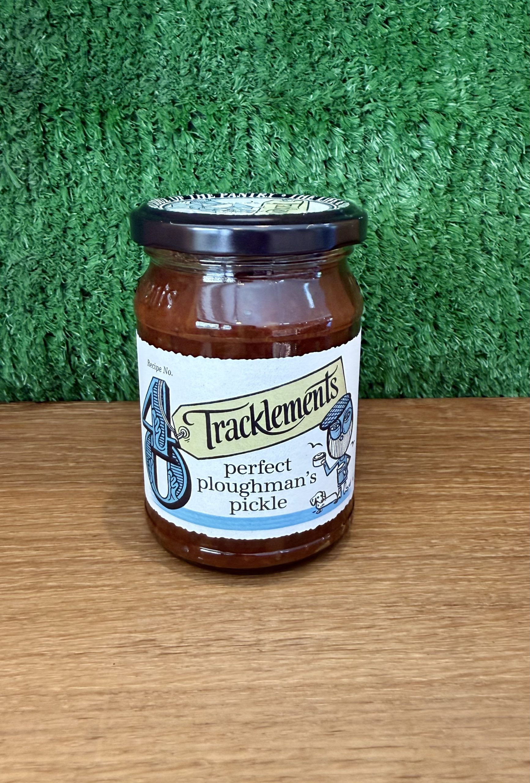 A photo of a jar of Perfect Ploughman's Pickle. It is pictured on a wooden board with a green background