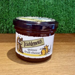 A picture of a jar of Tracklements Quince Fruit Cheese. It is positioned on a wooden board with a green background