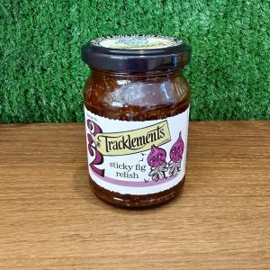 A jar of Sticky Fig Relish. It is pictured on a wooden board with a green background