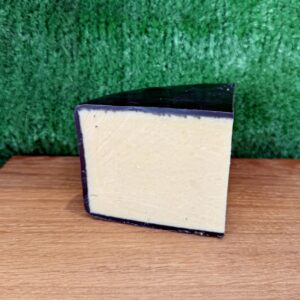 A picture of a wedge of Black Bomber cheddar. It is on a wooden board with a green background