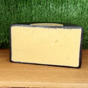 A picture of half a wheel of Dambuster cheddar cheese. It is sat on a wooden board with a green background