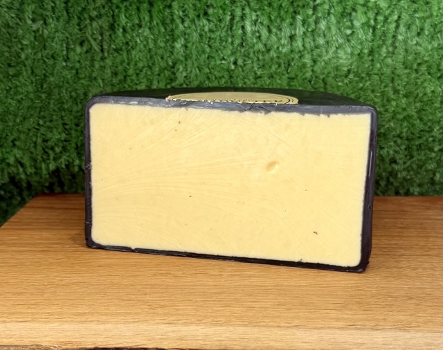 A picture of half a wheel of Dambuster cheddar cheese. It is sat on a wooden board with a green background