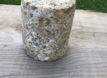 A picture of a Baby Colston Bassett Blue Stilton PDO. It is sat on a rustic wooden table.