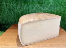 A picture of half a wheel of Bibury cheese. It is positioned on a wooden board with a green backdrop