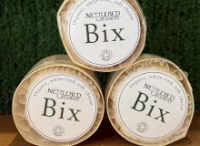 A photo showing 3 Bix cheeses arranged as a pyramid. They are positioned on a wooden board with a green background