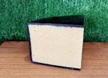 A picture of a wedge of Black Bomber cheddar. It is on a wooden board with a green background