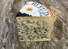 A picture depicting a wedge of Bleu D'Auvergne PDO Cheese. The cheese is positioned on a wooden table