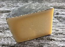 A picture of a wedge of Cornish Kern cheese. It is sat on a rustic wooden table.