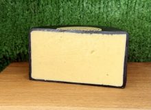 A picture of half a wheel of Dambuster cheddar cheese. It is sat on a wooden board with a green background