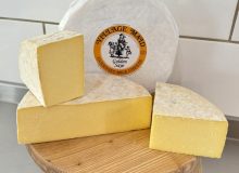 A picture of a display of Golden Saye cheese. There is a whole wheel plus cut pieces and they have been placed on a wooden board.