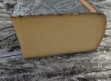 A picture of a wedge of Kaltbach Alpine Creamy cheese. It has been placed on a rustic wooden table.