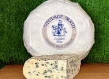 A picture showing a wedge of Loddon Blue. It is sat on a wooden board with a whole round of cheese propped up behind it
