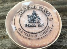 A picture of a round of Maida Vale Cheese. It is sat on a rustic wooden table