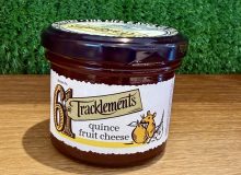 A picture of a jar of Tracklements Quince Fruit Cheese. It is positioned on a wooden board with a green background