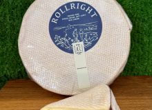 A picture showing a wheel of Rollright cheese with a cut wedge next to it. They are positioned on a wooden board with a green backdrop