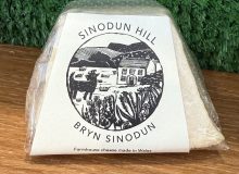 A picture of a Sinodun Hill cheese. This pyramid shaped cheese is positioned on a wooden board with a green background