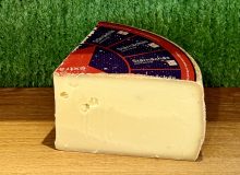 A picture of a wedge Stärnächäs Extra Mature cheese. It is shown on a wooden board with a green backgroud