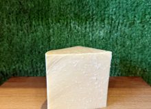 A picture of a wedge of Yorkshire Wensleydale PGI. It is positioned on a wooden board with a green background