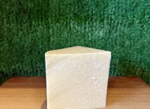 A picture of a wedge of Yorkshire Wensleydale PGI. It is positioned on a wooden board with a green background
