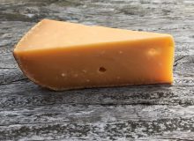 A picture of a wedge of 4 year old gouda. It is positioned on a wooden table