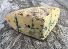 A picture of a wedge of Barkham Blue cheese. It is sat on a wooden table