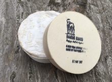 A picture of a 250g round cheese in a wooden box. It is sitting on a wooden table