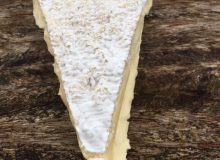 A picture showing a wedge of oozing Baron Bigod (a brie style cheese). It is depicted on a wooden table