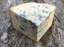 A picture of a wedge of Cashel Blue Cheese. It is positioned on a wooden table