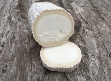 A picture showing a Chèvre Bûche Cheese. It has had a slice chopped which has been placed by the larger log. The cheese is positioned on a rustic, wooden table