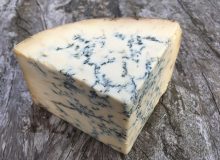 A wedge of Colston Bassett Blue Stilton PDO showing creamy texture and blue veining. Pictured on a wooden board
