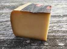 A wedge of Comté cheese sits on a wooden table