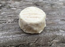A photo of a Crottin de Chavignol Cheese, placed on a rustic wooden table