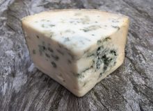 A picture depicting a wedge of Crozier Blue Cheese. It is positioned on a wooden table (and looks delicious!)