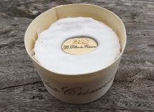 A picture of a whole Délice des Crémiers Baby Cheese. It is shown on a rustic wooden table