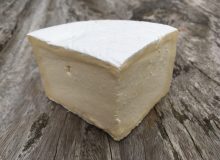 A picture of a wedge of Délice des Crémiers Cheese. It is shown on a rustic wooden table