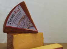 A picture showing 3 wedges of Dorset Red cheese. The cheeses are on a wooden table with the white background